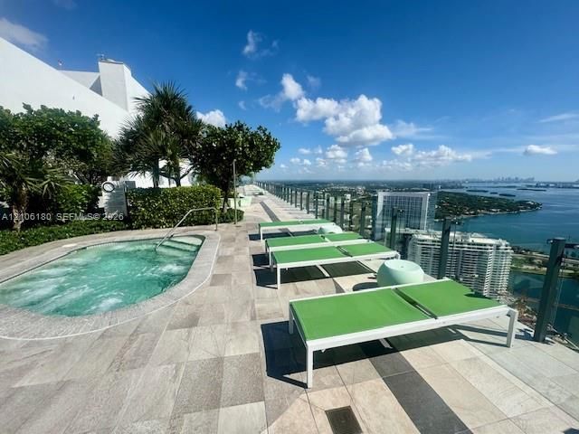 Rooftop terrace featuring a built-in spa, stone-tile decking, glass panel railing, and mature landscaping
