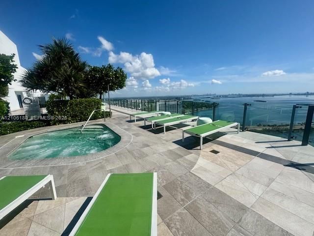 Rooftop terrace featuring an in-ground spa, stone tile decking, metal and glass railing, and mature landscaping