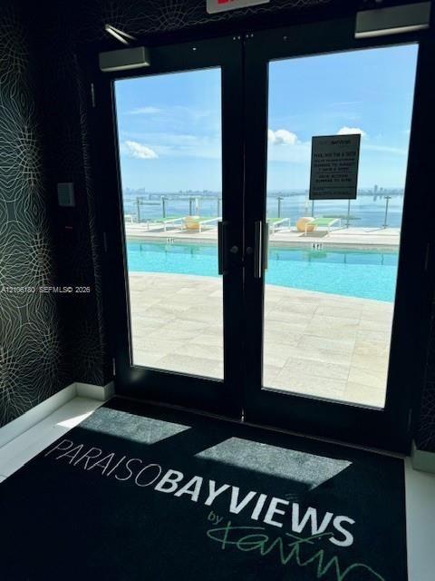 Double glass doors with black frames opening to an outdoor pool area with stone decking and a glass-paneled perimeter railing