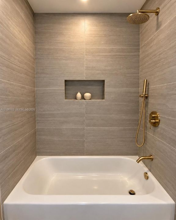 Bathtub with integrated shower featuring large-format tile surround, recessed wall niche, and brushed gold finish fixtures including a rainfall showerhead and handheld sprayer