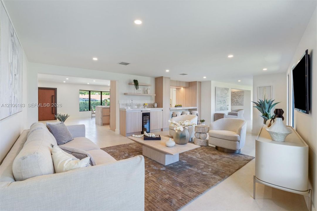 Open-concept interior featuring light-toned neutral flooring, recessed lighting, and a built-in wet bar with a glass-front beverage refrigerator and open shelving