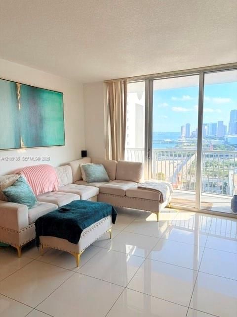 Polished ceramic tile flooring, floor-to-ceiling glass sliding doors, and a private balcony featuring a water and cityscape backdrop
