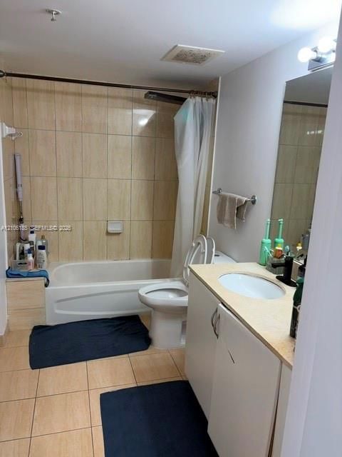 Full bathroom featuring porcelain tile flooring, a tub-shower combination with floor-to-ceiling tile surround, a vanity with a solid surface countertop, and a wall-mounted light fixture