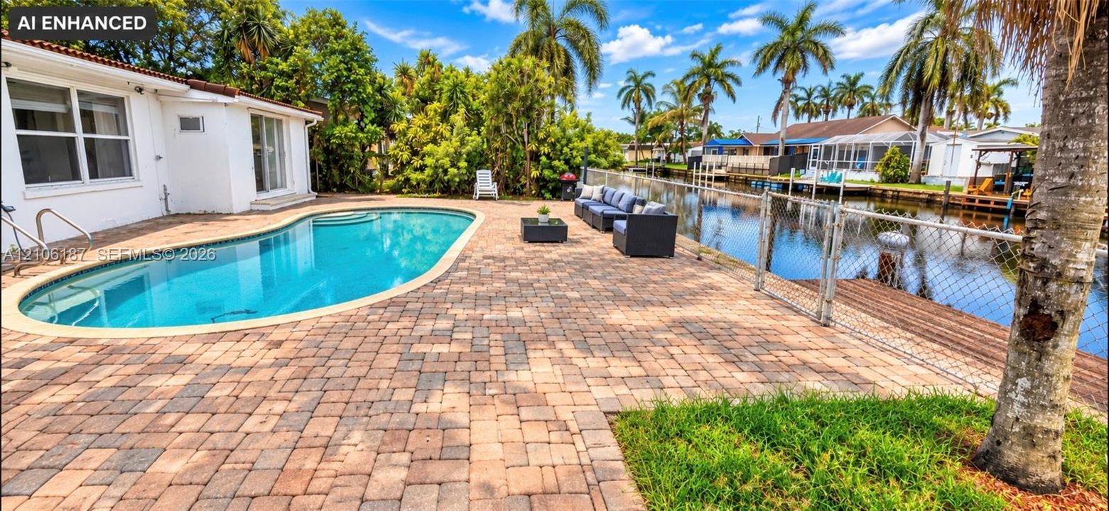 In-ground swimming pool with brick-paver patio, wooden bulkhead, and waterfront access