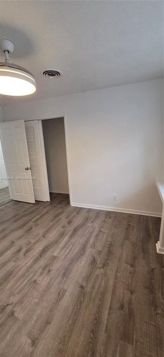 Interior space featuring wood-finish flooring, a neutral color palette, built-in closet with louvered doors, and a central ceiling-mounted light fixture