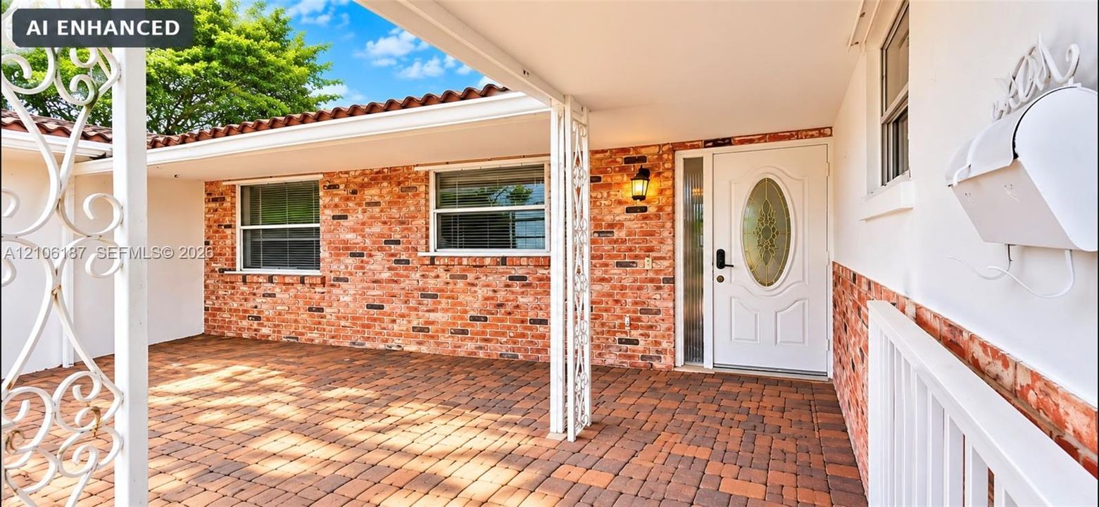 Covered front entry featuring red brick exterior siding, terracotta-style roof tiles, decorative metal porch supports, and a paved brick porch