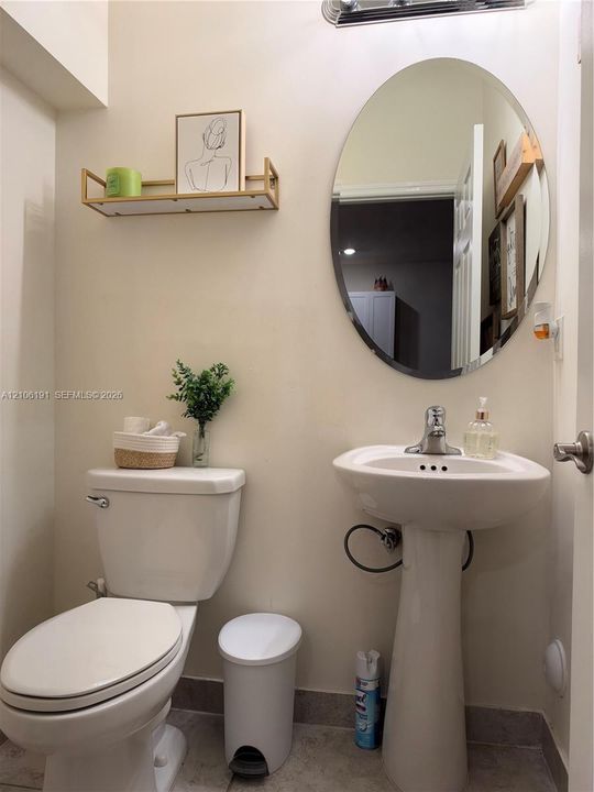 Pedestal sink with a single-handle faucet, oval wall-mounted mirror, and wall-mounted metal shelf