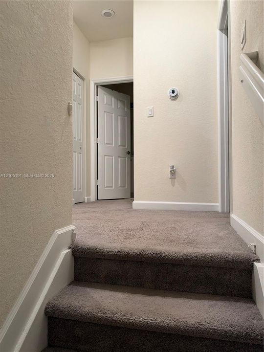 Neutral carpeted flooring, white six-panel interior doors, and wall-mounted digital thermostat