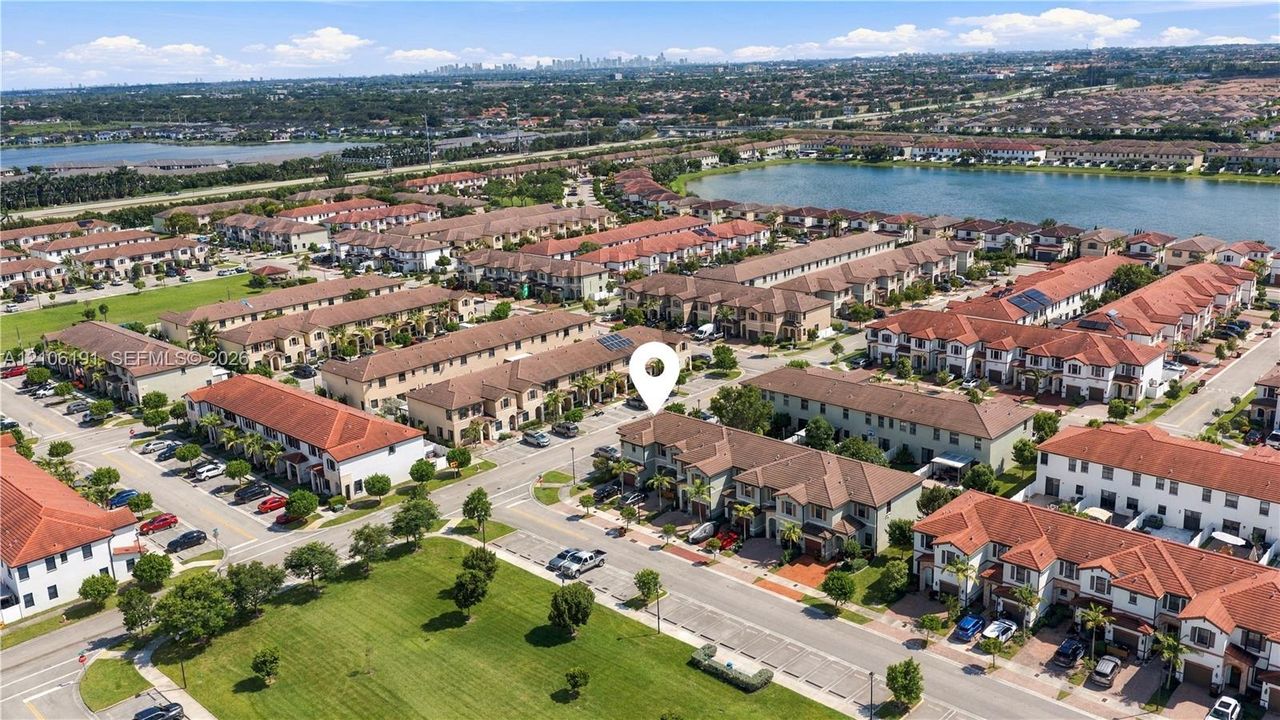 Aerial perspective of a multi-story residence featuring a terracotta-tiled roof and stucco exterior, situated within a community highlighted by expansive water frontage and manicured green spaces