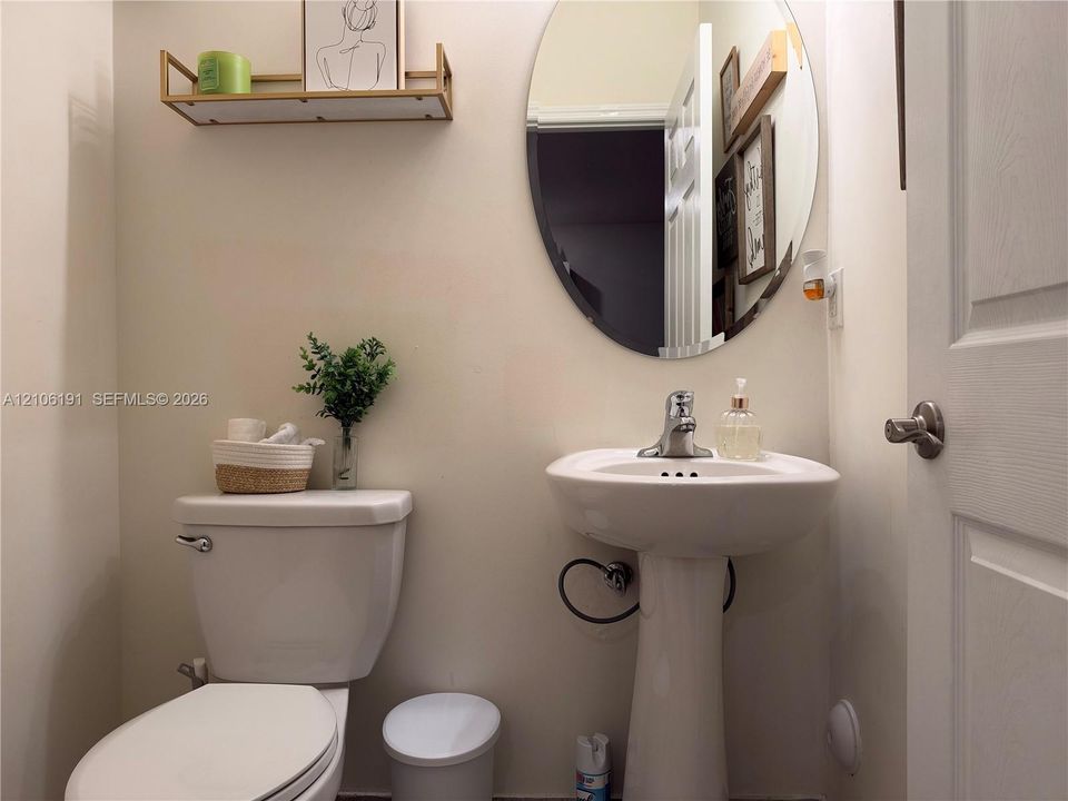 Oval wall-mounted mirror, white pedestal sink with chrome faucet, and fixed wall-mounted shelving