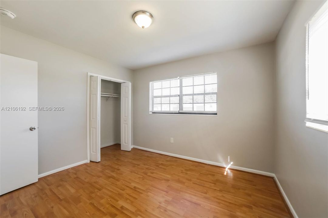 Room featuring wood-finish flooring, neutral wall paint, a multi-pane window with white trim, and a closet with bifold doors