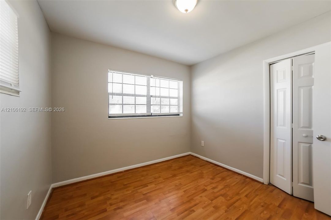 Room featuring wood-finish flooring, neutral wall paint, a multi-pane window, and a closet with paneled bifold doors