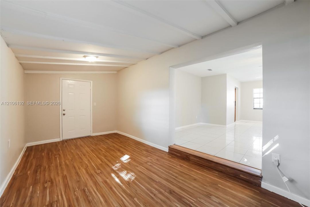 Wood-finish flooring, tray ceiling with exposed structural beams, raised threshold, and large-format tile flooring