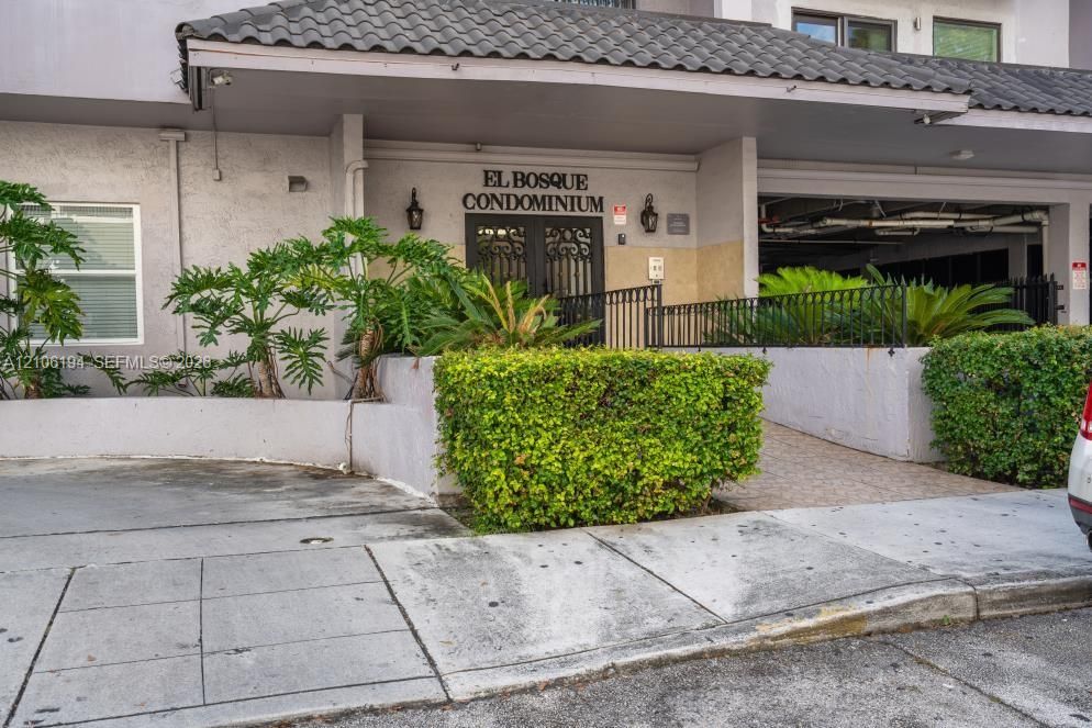 Exterior facade featuring a covered entryway with decorative metal double doors, tile roofing, integrated wall-mounted lighting, and curated shrubbery
