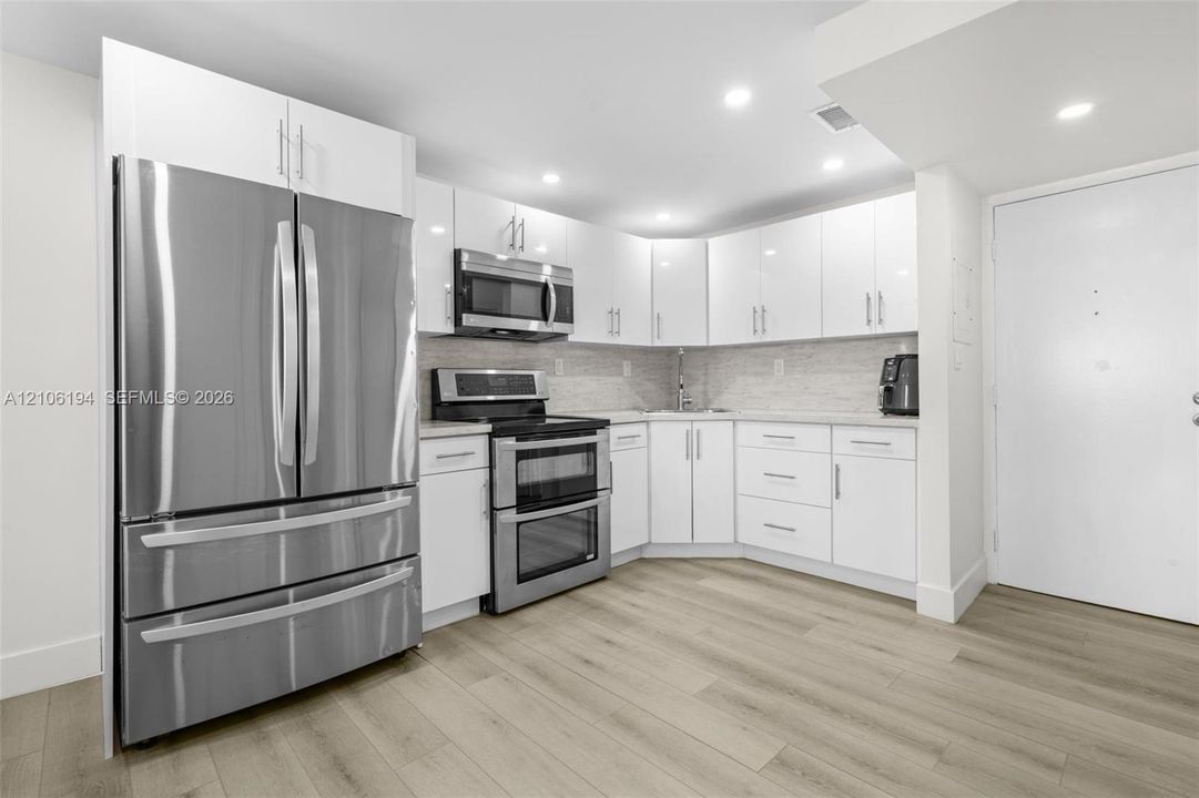 Kitchen featuring white cabinetry, stainless steel appliances,laminate wood-finish flooring, recessed lighting, and a light-toned backsplash