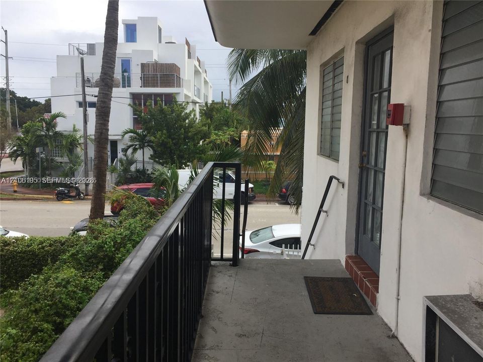 Exterior balcony featuring a concrete floor, black metal railing, and a multi-pane glass-panel entry door