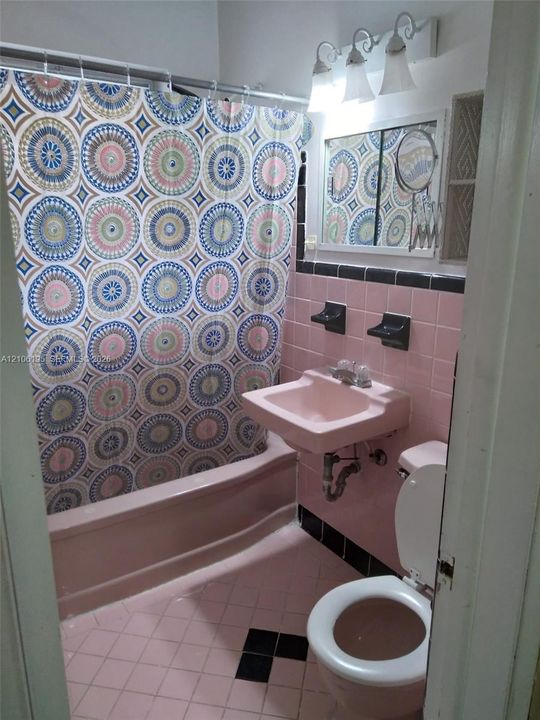 Bathroom featuring pink wall tiling with black accent trim, wall-mounted sink, built-in shelving, and a three-light vanity fixture