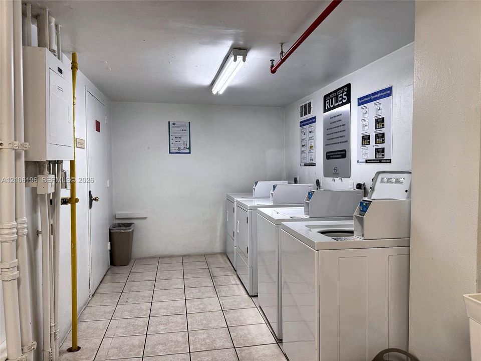 Laundry center featuring multiple side-by-side washers and dryers, tiled flooring, and industrial-style exposed piping