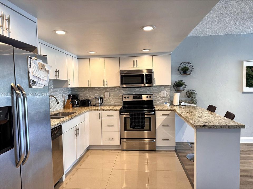 Kitchen featuring white cabinetry, stone-finish countertops, stainless steel appliances, a breakfast bar, and tile flooring