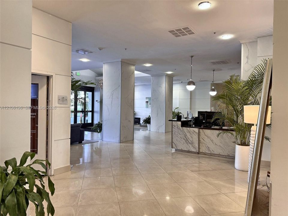 Common area featuring large-format tile flooring, stone-surfaced reception desk, structural columns with decorative stone cladding, and pendant lighting