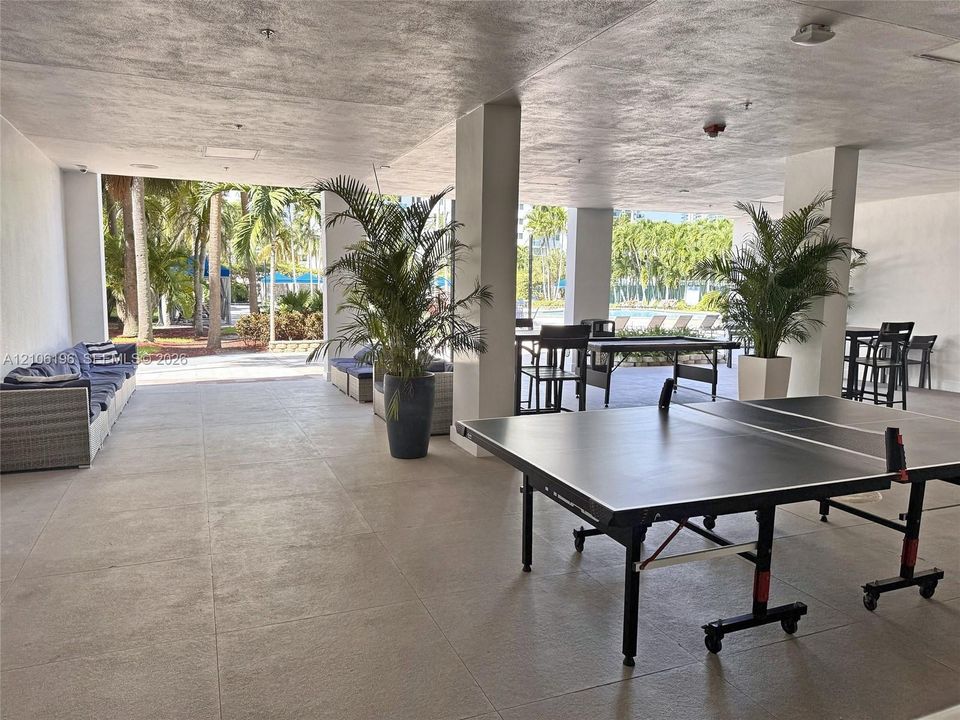 Covered outdoor recreation space featuring structural columns, large-format tile flooring, and expansive open-air access