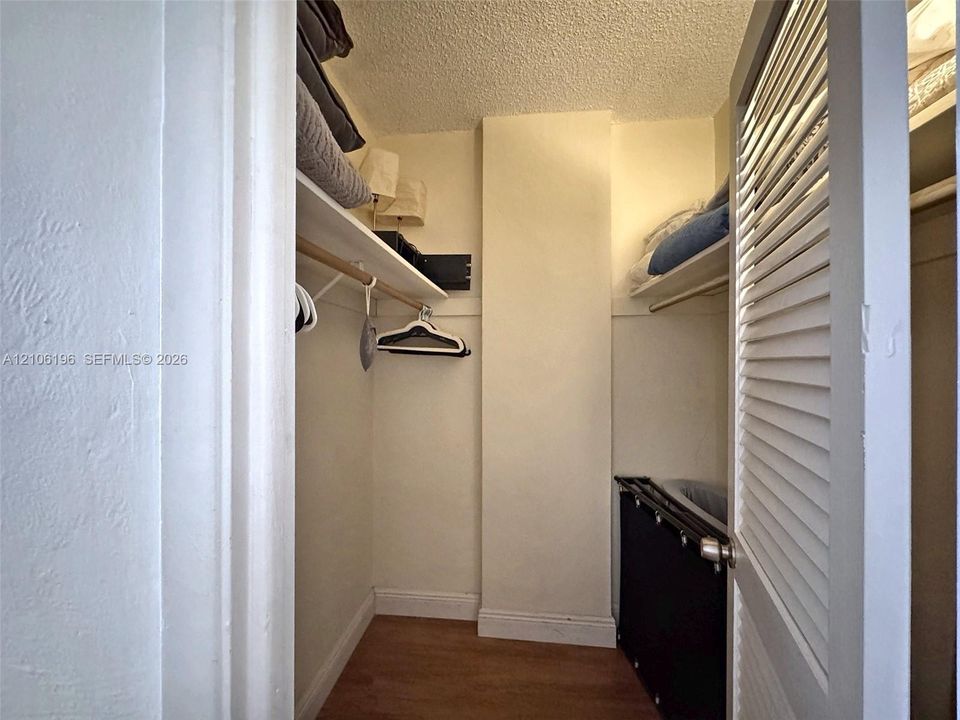 Storage closet featuring wood-finish flooring, dual-tier shelving, wooden hanging rods, and louvered swinging doors