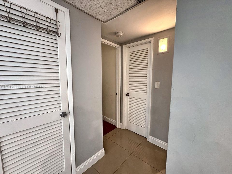 Neutral-toned interior featuring large-format tile flooring, white louvered closet doors, and a wall-mounted sconce