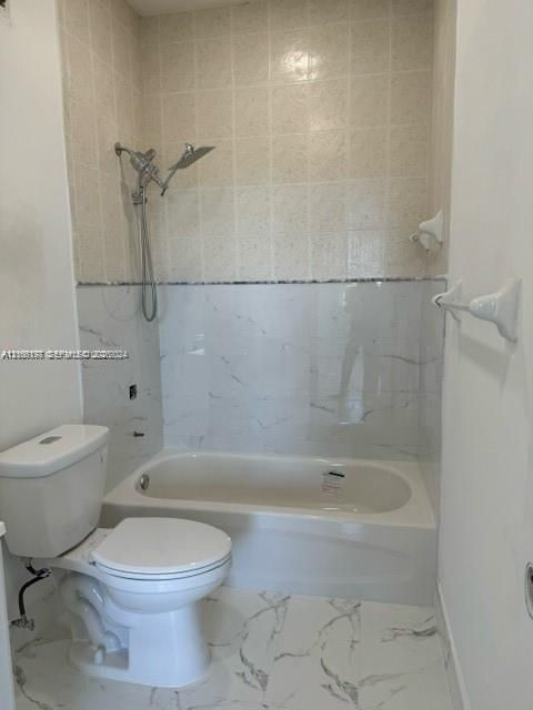 Bathtub featuring stone-pattern wall tile, hand-held shower fixture, and stone-pattern floor tile