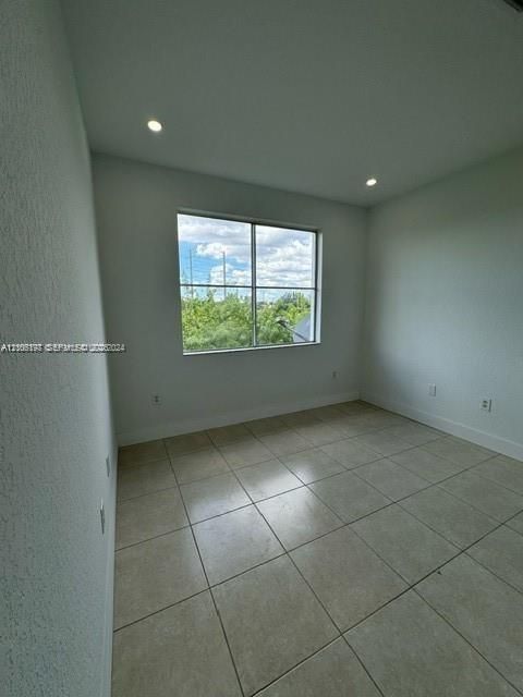 Neutral-toned room featuring large-format tile flooring, recessed ceiling lighting, and a window with exterior greenery