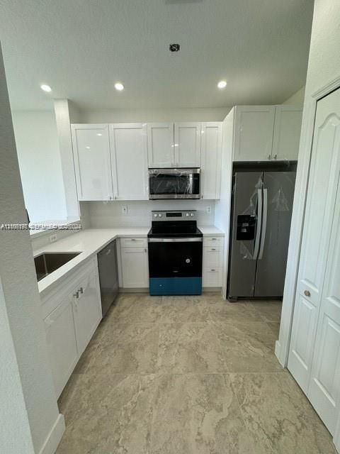 Kitchen featuring white shaker-style cabinetry, solid-surface countertops, large-format tile flooring, stainless steel appliances, and a recessed sink