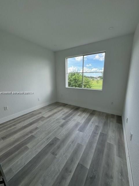 Neutral-toned interior space featuring wood-finish flooring, recessed lighting, and a large window with exterior greenery