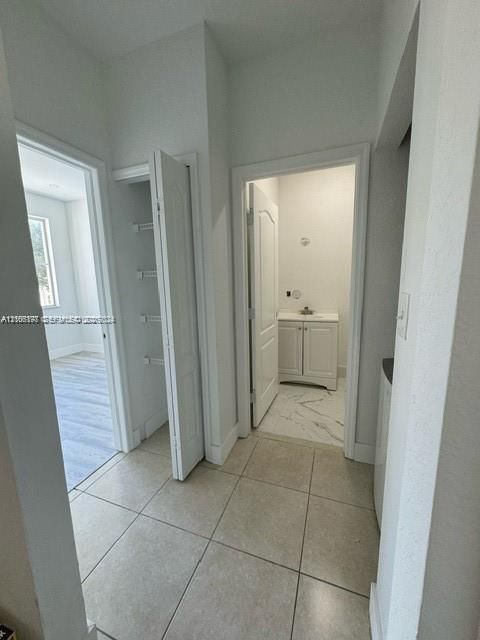 Hallway featuring large-format tile flooring, a dedicated storage closet with built-in shelving, and entry to a bathroom finished with light stone-patterned flooring and a vanity cabinet