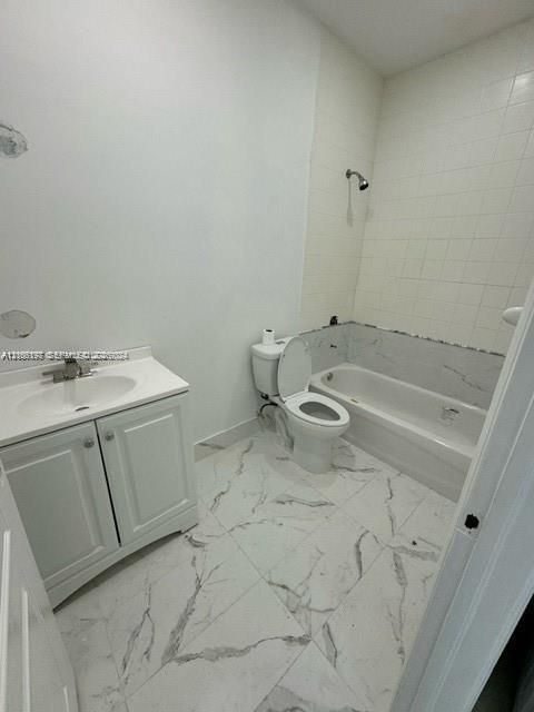 Bathroom featuring large-format white tile flooring with grey veining, a white vanity with an integrated sink, a porcelain toilet, and a bathtub with tile surround