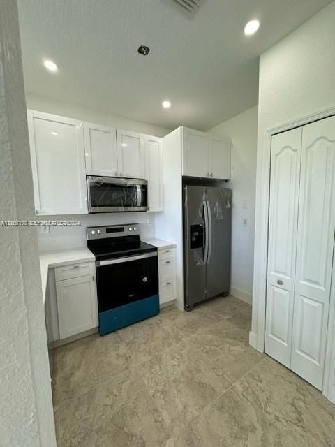 Kitchen featuring white shaker-style cabinetry, stainless steel appliances, quartz-surface countertops, and ceramic tile flooring