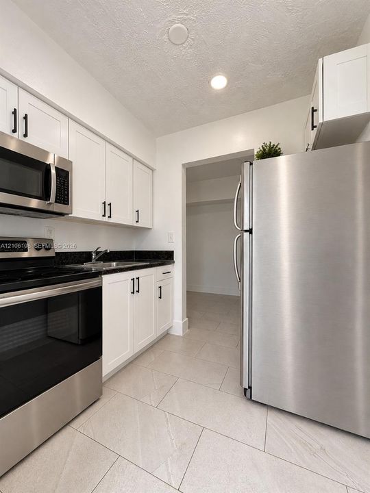 Kitchen featuring white cabinetry with matte black hardware, dark stone-finish countertops, stainless steel appliances, and large-format tile flooring