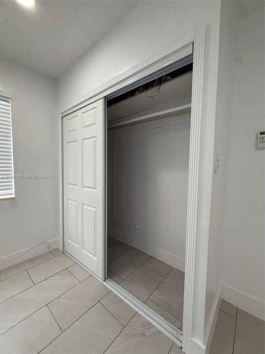 Closet featuring six-panel sliding doors, overhead rod, and large-format tile flooring