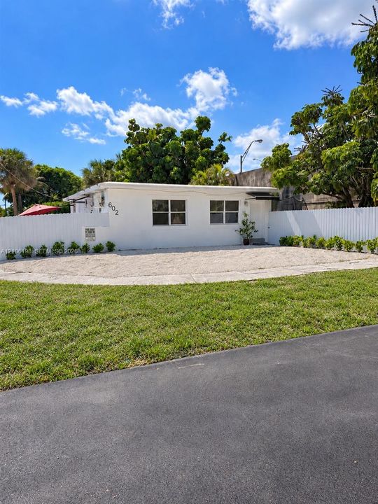 Single-story residence featuring a crisp white exterior, gravel front courtyard, horizontal slat privacy fencing, and manicured lawn