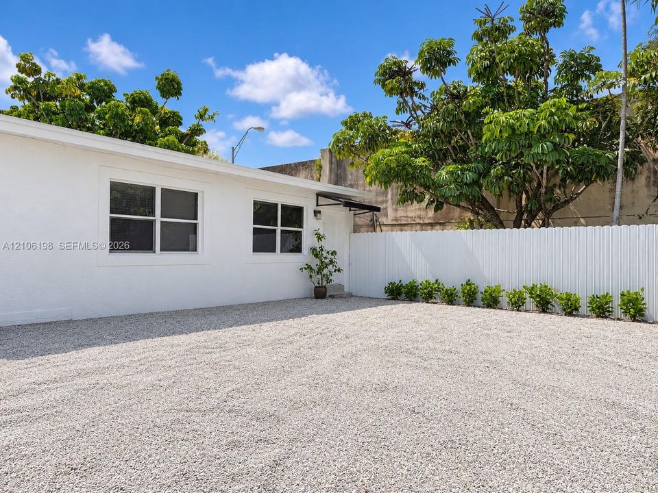 Exterior featuring a white stucco facade, gravel ground cover, and a white privacy fence accented by mature landscaping