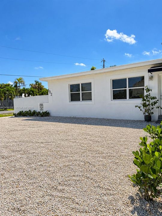 Exterior featuring a white stucco facade, gravel driveway, and white vinyl privacy fencing