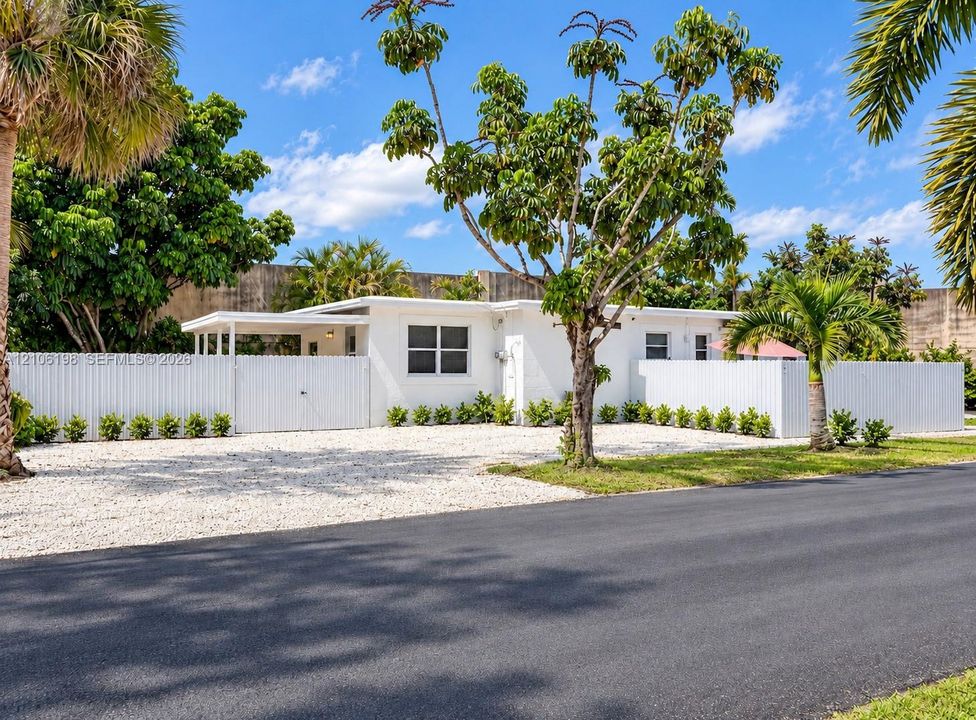 Single-story residence featuring white exterior cladding, a covered entryway, an expansive gravel front area, and a privacy fence