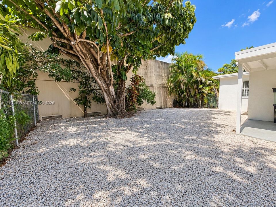 Low-maintenance gravel yard featuring a concrete patio, mature shade tree, and perimeter fencing