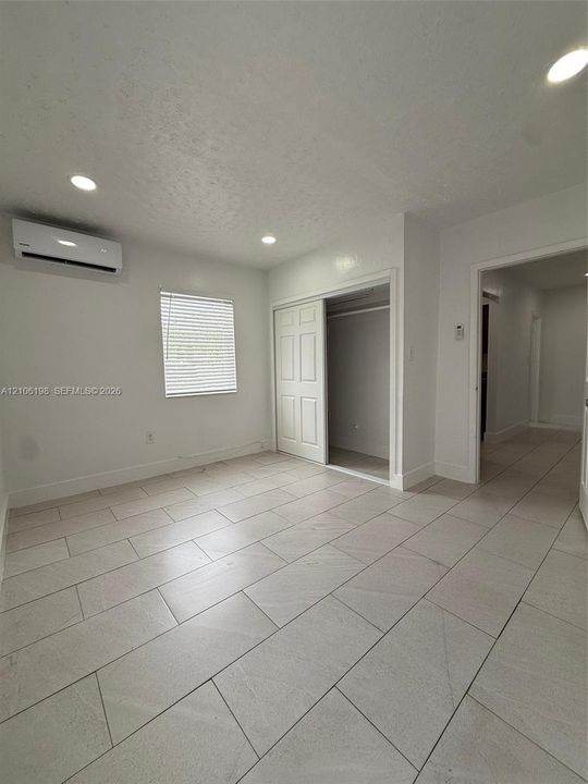 Neutral-toned tile flooring, recessed ceiling lighting, wall-mounted ductless climate control unit, and sliding closet doors