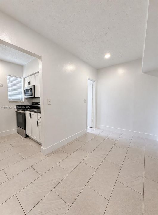 Neutral-toned large-format tile flooring, white cabinetry, integrated stainless steel appliances, and recessed lighting