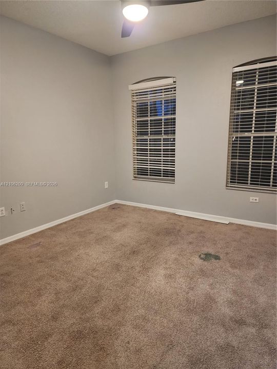 Neutral-toned walls featuring arched windows with integrated blinds, wall-to-wall carpeting, and a ceiling fan