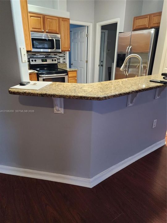 Kitchen featuring a peninsula with a stone-surfaced breakfast bar, stainless steel appliances, wood-finish cabinetry, and wood-finish flooring