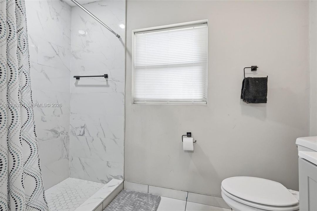 Full-height shower surround with stone-patterned tile, white hexagonal tile shower flooring, recessed window with blinds, and matte black hardware