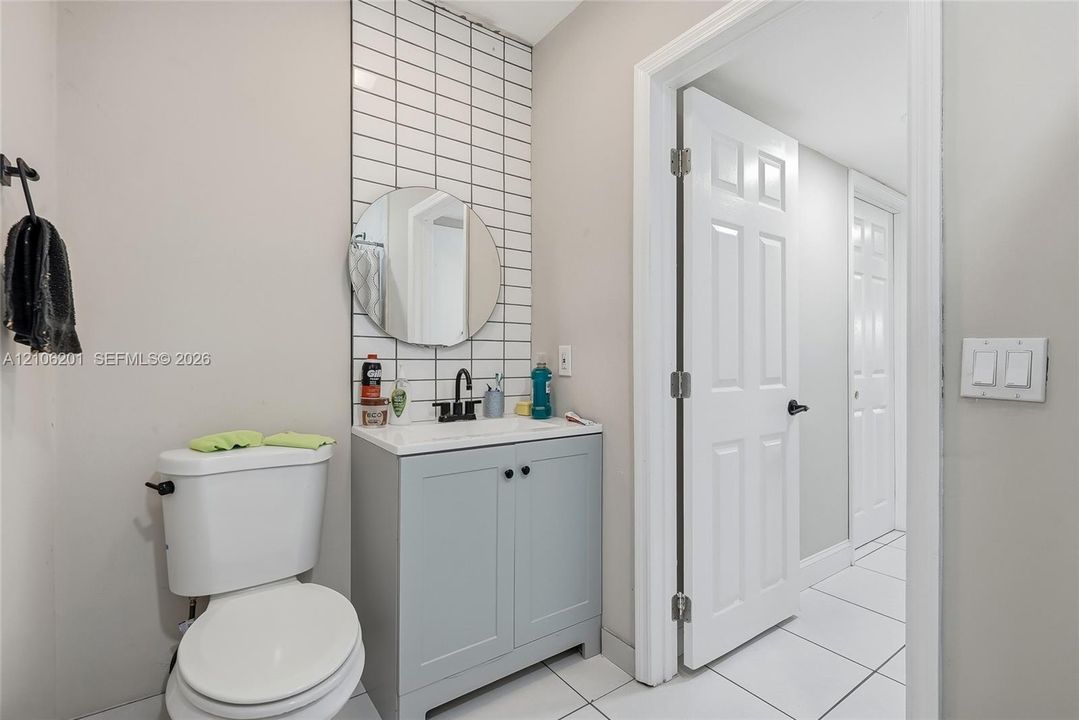 Bathroom featuring a light blue vanity, rectangular white sink with a matte black faucet, circular wall-mounted mirror, and vertical white tiled backsplash