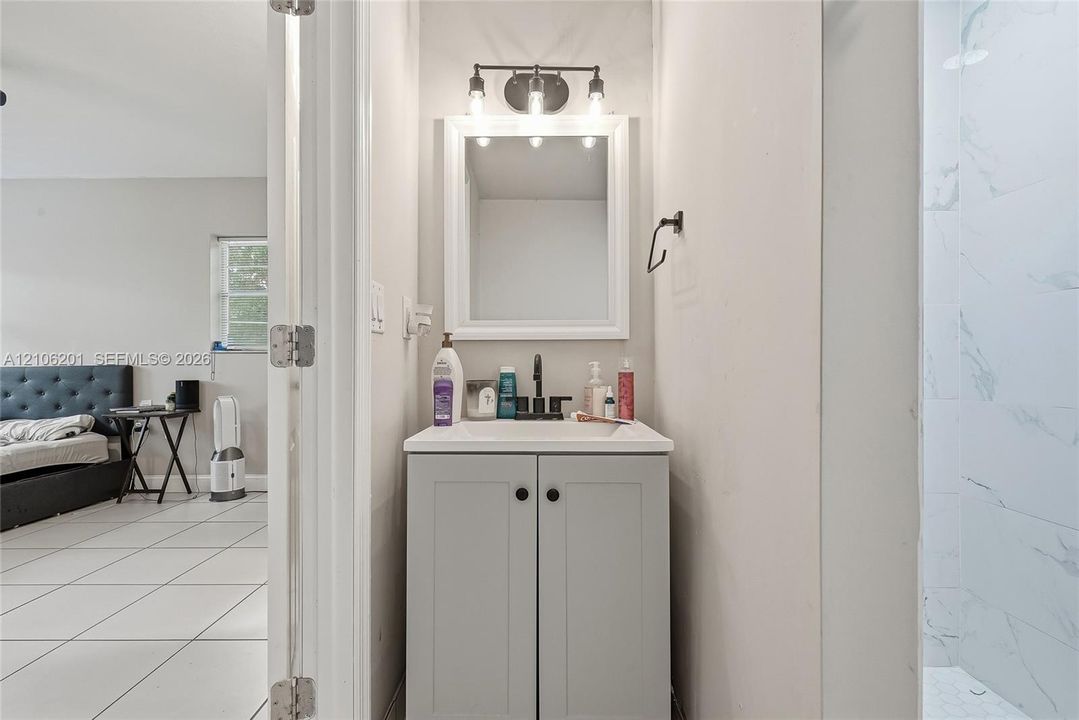 Light grey Shaker-style vanity with a rectangular sink, matte black faucet, framed mirror, and three-bulb vanity light fixture