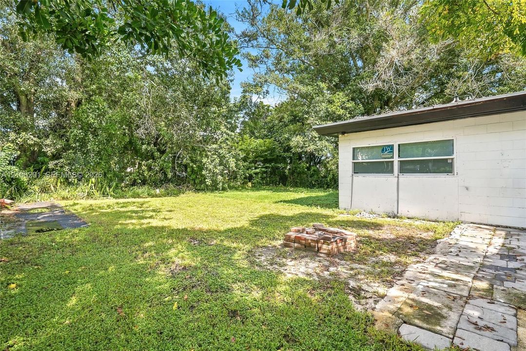 Spacious backyard featuring a brick fire pit, stone paver pathway, and mature tree canopy