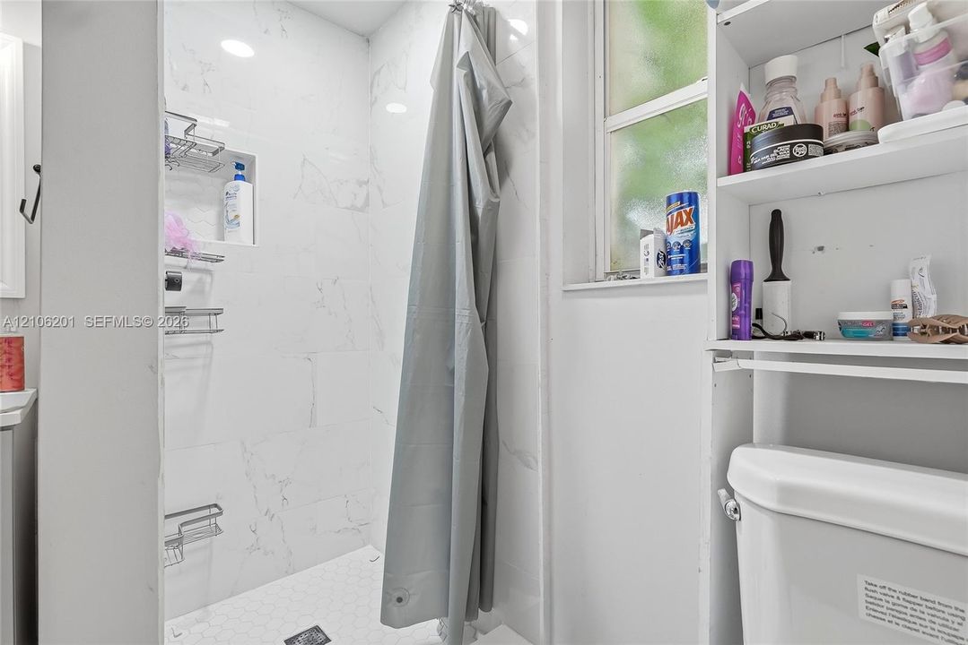 Shower enclosure featuring large-format white stone-finish wall tile, a recessed storage niche, and a hexagonal tile floor